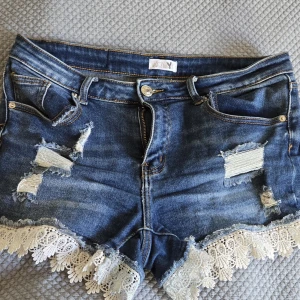 Blå jeansshorts med spets - Snygga blå jeansshorts, midwaist från Hailys med slitna detaljer och vit spetskant längst ner. Klassisk femficksmodell med knapp och dragkedja framtill. Jätte snygga och jättesköna att ha på sig då dom har stretch! Stl M men passar mellan S-L då den har strech! Snygga detaljer som gör så att dom ser lite snyggare ut! Skriv om du har några frågor, skriv om du vill köpa eller är intresserad!! Pris går att diskuteras! 🫶