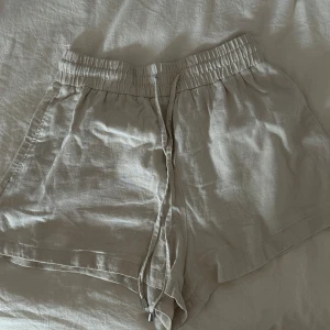 Beige linneshorts från Zara  - Snygga beige shorts från Zara i storlek XS, men är lite större nu tycker jag och de har resårband. Tillverkade i mjukt linne. De har en elastisk midja med snörning för skön passform och en loose siluett. Perfekta för varma dagar och chill stil. Färgen är ljusbeige och materialet känns luftigt och fräscht.