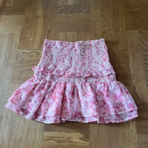 Rosa blommig volangkjol - Supersöt kort kjol i rosa och vitt med blommigt mönster och volanger. 