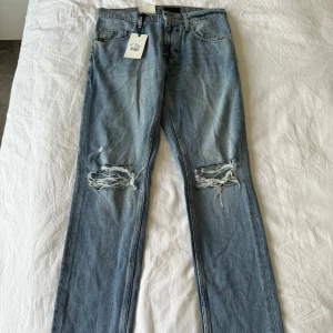 Tiger of Sweden jeans, oanvända med tags kvar på. - Säljer ett par ljusblå jeans från Tiger of Sweden i storlek 29/32. Jeansen har raka ben och hål över båda knäna. Klassisk femficksmodell. Oanvända med tags kvar. 