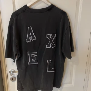 Axel arigato T-shirt  - Cool t-shirt i storlek m men är en oversized modell med stora bokstäver AXEL på ryggen. Tjockare bomullstyg och klassisk rund hals. Perfekt för dig som gillar streetstyle och vill sticka ut med ett unikt tryck.