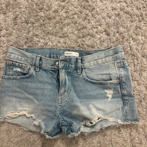Ljusblå jeansshorts från Perfect Jeans - Säljer ett par ljusblå jeansshorts från Perfect Jeans med fransiga och slitna detaljer vid bensluten. Klassisk femficksmodell med bälteshällor och knappstängning. Perfekt för dig som gillar en avslappnad och trendig stil.