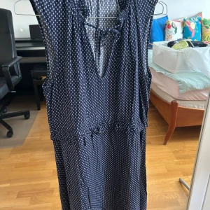 Mörkblå prickig klänning från H&M - Supersöt mörkblå klänning från H&M med vitt prickigt mönster, ärmlös design och knytning vid halsen. Klänningen har en avslappnad passform och lätt rynk vid midjan. Perfekt för varma dagar och enkel att styla med sneakers eller sandaler.