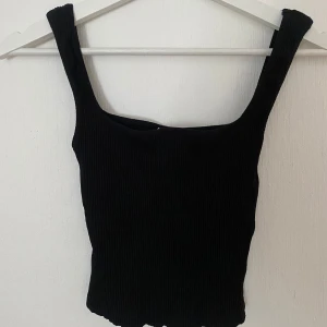 Svart ribbad linnetopp från NA-KD - Svart ribbad linnetopp från NA-KD Reborn med breda axelband och fyrkantig ringning. Toppen är figurnära och har en enkel, stilren look som passar perfekt till jeans eller kjol. 