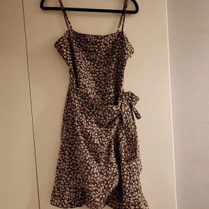 Blommig omlottklänning med knut - Supersöt klänning i omlottmodell med rosablommigt mönster. Klänningen har en feminin passform och passar perfekt till alla sommartillfällen ☀️🍹