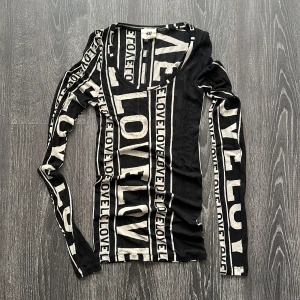 Svartvit långärmad topp H&M Studio - Snygg långärmad topp från H&M Studio i svart och vitt med coolt grafiskt LOVE-tryck över hela tröjan. Tunn och stretchig i materialet, med rundad ringning och figurnära passform. Perfekt för dig som gillar statement-plagg och streetstyle.