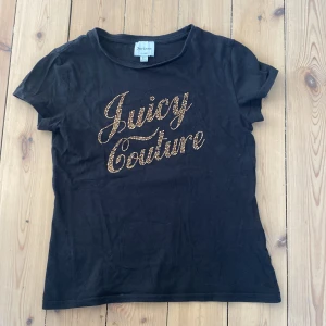 Svart Juicy Couture t-shirt med guldtext - Svart t-shirt från Juicy Couture med korta ärmar och rund hals. Framsidan har en stor glittrig Juicy Couture-logga i guld. T-shirten är i en klassisk passform som är enkel att styla till jeans eller kjol. Använt den sparsamt💞