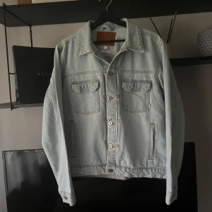Ljusblå jeansjacka  - Snygg ljusblå jeansjacka från Woodbird i klassisk modell med krage, två bröstfickor med lock och knappar framtill. Jackan är tillverkad i bomull och har raka ärmar och en clean look som funkar till många stilar. Jackan är aldrig någonsin använd och är som helt ny. Köptes för runt 1200kr men säljer för 300kr - bra deal enligt mig. Passar mig perfekt som är ca 180cm och väger runt 70kg.