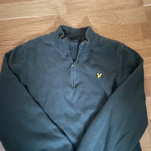 Mörkgrå half zip tröja Lyle & Scott - Snygg mörkgrå långärmad tröja från Lyle & Scott med klassisk gul logga på bröstet. Tröjan har en ribbad krage och praktisk half zip-dragkedja framtill. Perfekt för dig som gillar stilren och enkel design. Storlek 14-15 men stämmer ej det passar 11-13 152-158 har krympt.  