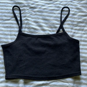 Svart ribbad magtröja - Svart croppad linnetopp från H&M i storlek S med smala axelband och ribbad struktur. Perfekt till jeans eller kjol för att få en enkel och stilren outfit
