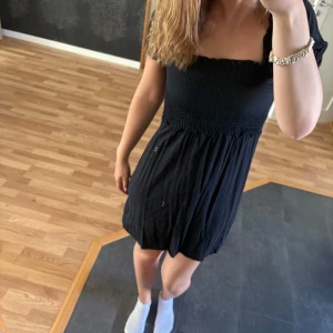 Svart kort klänning med smock - Supersöt svart klänning med smock upptill och luftig kjol.  Materialet känns lätt och bekvämt mot huden.