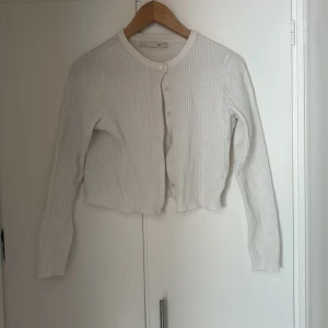Vit ribbad kofta  - Säljer en vit ribbad kofta med rund hals och knappar framtill. Koftan är croppad och har långa ärmar. Strl S