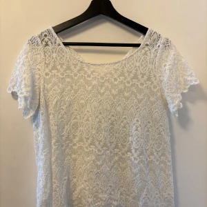 Vit lace top - Säljer en elegant vit spetsblus med korta ärmar. Blusen har ett vackert spetsmönster som ger en romantisk känsla. Perfekt för sommarens alla tillfällen.