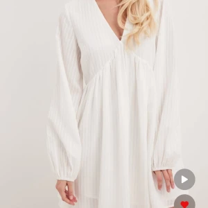 Vit klänning från Na-Kd - Säljer en stilren vit klänning från Na-Kd med v-ringning och långa ärmar. Klänningen har en luftig passform och ett subtilt randigt. Aldrig använd💕