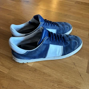 Valentino Flycrew i Storlek 46 - Snygga och eftertraktade sneakers från Valentino i blå mocka med vita detaljer. Skorna har en klassisk design med snörning och rund tå. Perfekta för en stilren look.                           Storlek: 46                                                                         Nypris: 7000                                                                    Mitt pris: 2699