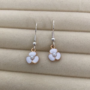 Blomformade örhängen med pärldetalj - Charmiga örhängen i form av blommor med vit emalj och en liten pärla i mitten. De har en elegant guldtonad kant och hängs på en krok av silverfärgad metall.