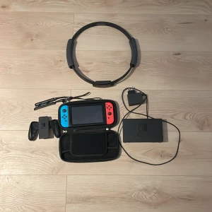 Nintendo Switch med Ring Fit Adventure - Säljer en Nintendo Switch med blå och röd Joy-Con, dockningsstation, handkontroll och Ring Fit Adventure-tillbehör. Perfekt för både spel och träning. Inkluderar även laddare och bärväska. Allt du behöver för en komplett spelupplevelse! 🎮 man får även med några spel