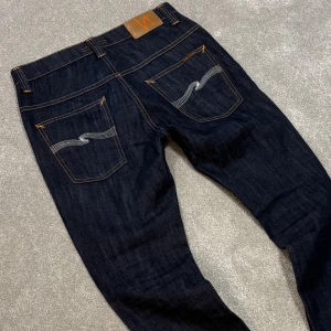 Nudie Jeans - Tja! Säljer dessa riktigt snygga mörkblå Nudie jeans med vit swoosh! Jeansen är utav modellen ”Thin Finn” och har en slim/straight passform. Size 31/32. Skriv vid funderingar!