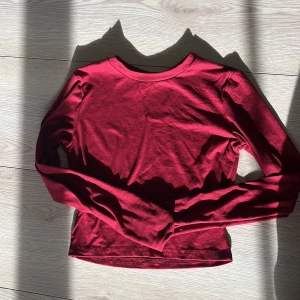 Röd långärmad topp från SHEIN - Snygg röd långärmad topp från SHEIN i ett mjukt och stretchigt material. Perfekt för en stilren look. Tillverkad i polyester och elastan för en bekväm passform.