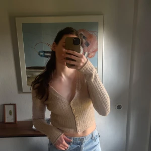 Beige ribbad kofta - Säljer en stilren beige ribbad kofta med v-ringning och knappar framtill. Koftan är croppad och har långa ärmar, perfekt för en avslappnad look. Passar bra till jeans eller kjol. Köpt i butik i Italien!