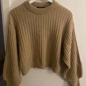 Beige ribbad tröja från Gina Tricot - Säljer en snygg beige ribbad tröja från Gina Tricot. Tröjan har en croppad passform med långa ärmar och rund halsringning. Perfekt för en stilren look! 💫