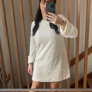 Creamfärgad paljettklänning med svart rosett - Säljer glittrig klänning med paljetter och en stor svart rosett på baksidan som man kan styla själv Använd 1 gång (tvättad men en smink rand på insidan av halsen) ⚠️161 cm lång⚠️