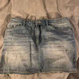 Jeanskjol i ljusblå denim - Snygg jeanskjol i ljusblå denim. Kjolen har en kort längd och stängs med dragkedja och knapp framtill. 