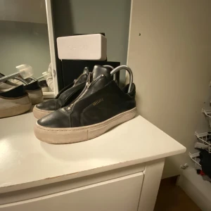 Svarta sneakers från Axel Arigato - Snygga svarta sneakers från Axel Arigato med dragkedja framtill. Skorna har en stilren design med en vit sula och är tillverkade i skinn. Perfekta för en trendig look.