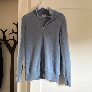 Ljusblå kashmirtröja från Soft Goat - Säljer en elegant ljusblå kashmirtröja från Soft Goat. Tröjan har en dragkedja framtill och långa ärmar. Den är mjuk och bekväm med ribbade kanter vid ärmslut och nederkant. Priset är inte hugget i sten!