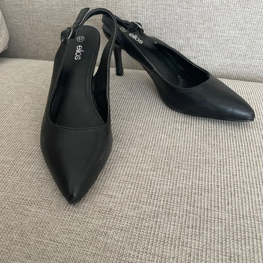 Snygga svarta pumps från Ellos med spetsig tå och smal klack. Perfekta för en elegant look. De har en stilren design med en justerbar rem runt hälen.. Kengät.