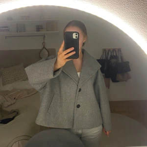 Grå kappa från VeroModa - Grå kappa från veromoda med en krage och knappar framtill. Jackan har en jättefin passform och är lagom varm både till sommaren och hösten. Lite stor i modellen
