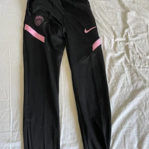 Svarta träningsbyxor från Nike med PSG-logga - Psg byxor vet inte direkt vilken storlek men passar den som är 145-155 skulle jag säga. Ett litet hål i fickan 