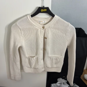 Vit stickad kofta med knappar - Säljer en stilren vit stickad kofta med rund hals och knappar framtill. Koftan har långa ärmar och två praktiska fickor. Perfekt för en mysig och elegant look.