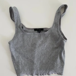 Grå ribbad linnetopp från Forever 21 - Säljer en stilren grå ribbad linnetopp från Forever 21. Toppen har breda axelband och en croppad passform som ger en trendig look. Perfekt för varma dagar eller som lager under en jacka. 🩶