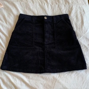 Marinblå manchesterkjol - Snygg marinblå manchesterkjol med fickor fram och knappstängning. Perfekt för en stilren look. Kjolen har en klassisk A-linjeform och är gjord i ett mjukt manchestermaterial. Storlek 38 men passar som 34/36. Aldrig använd.