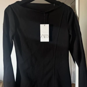 Svart klänning från Zara - Snygg svart klänning från Zara med långärmad design. Perfekt för en stilren look. Klänningen har en enkel och elegant stil som passar till många tillfällen.