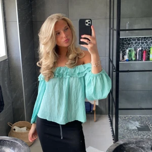 Mintgrön offshoulder blus - Säljer en söt mintgrön offshoulder blus med volangdetaljer. Blusen har långa ärmar med elastiska muddar och en luftig passform. 