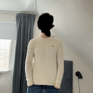 Vit kabel stickad från Morris - Säljer en stilren vit stickad tröja från Morris  med en liten diskret logga på bröstet. Tröjan har ett klassiskt flätmönster och långa ärmar. 
