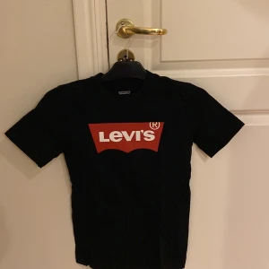 Svart t-shirt från Levi's - Snygg svart t-shirt från Levi's med det klassiska röda logotyptrycket på bröstet. Perfekt för en avslappnad stil. Tillverkad i mjukt material för extra komfort.