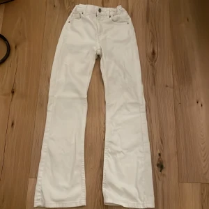 Vita bootcut jeans - Snygga vita bootcut jeans med mid midja och klassisk femficksdesign. Byxorna har en knapp och dragkedja framtill samt bälteshällor. Perfekta för en stilren look.
