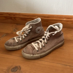 Höga sneakers från Converse  - Säljer ett par beige höga sneakers från Converse med snörning och mjukt foder. Skorna har en klassisk rund tå och är tillverkade i mocka. Perfekta till våren! 