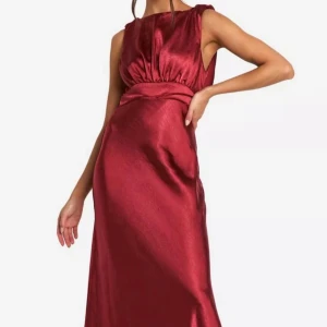 Vinröd långklänning med öppen rygg - Elegant vinröd långklänning i satin med en vacker öppen rygg och knytband. Klänningen har en ärmlös design och en smickrande passform som passar perfekt för festliga tillfällen. Är storlek 36 men jag skulle säga att den är liten i storleken. Jag brukar ha 34 och den passade mig perfekt. Klänningen är helt ny och aldrig använd. Passar perfekt till balen😍