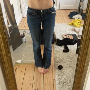 Blå bootcut jeans med broderad detalj - Säljer ett par snygga blå bootcut jeans med broderad detalj på bakfickorna. Jeansen har en låg midja och klassisk femficksdesign. Perfekta för en avslappnad stil.