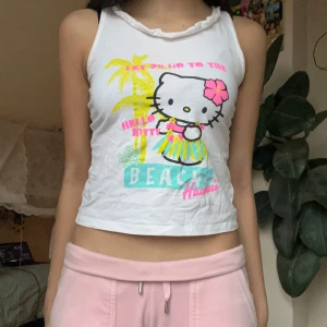 Vit Hello Kitty linnetopp - Söt vit linnetopp med Hello Kitty-tryck och färgglada detaljer. Perfekta baby toppen med gulligaste trycket! Tillverkad i bomull 💞