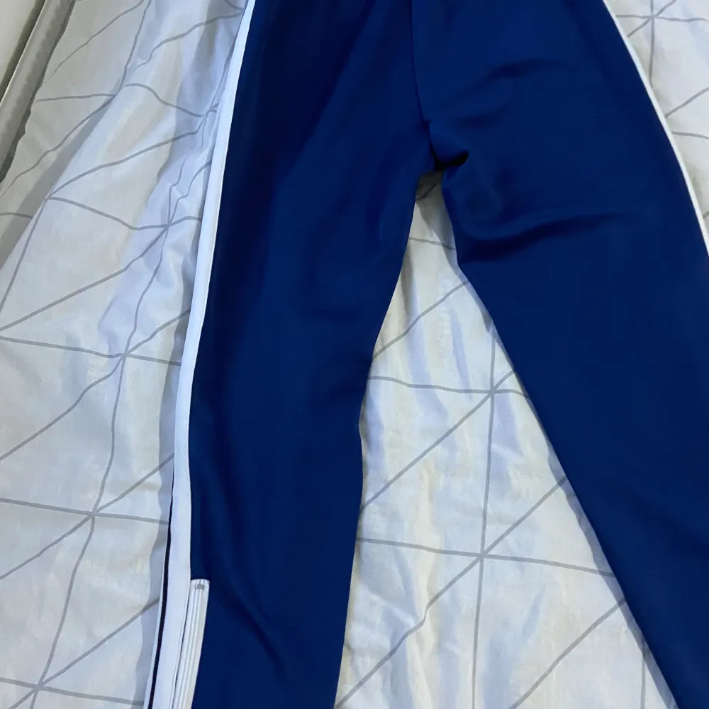 Snygga blå träningsbyxor från Palm Angels med vita sidoremsor och logotyp på framsidan. Byxorna har en elastisk midja med snörning för bästa passform. Perfekta för en sportig look!. Farkut & Housut.