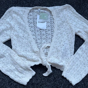 Vit spetskofta från ONLY - Säljer en söt vit spetskofta från ONLY med knytning framtill. Koftan har långa ärmar och ett fint hålmönster som ger en romantisk känsla. Perfekt för lager-på-lager-stil eller sommarens svalare kvällar. 🌸