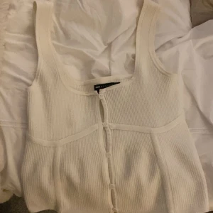 Vit ribbad linnetopp från Zara - Säljer en stilren vit ribbad linnetopp från Zara. Toppen har breda axelband och knappar framtill som ger en snygg detalj. Perfekt för varma dagar eller som ett lager under en jacka.