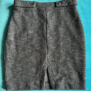 Grå kjol från Guess - Snygg grå kjol från Guess med en stilren design. Kjolen har en slits framtill och dekorativa knappar i midjan. Perfekt för en chic look!