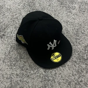 Svart keps från New Era - Snygg svart keps från New Era med klassisk logga framtill och texten 'Love & Hustle Game' baktill. Kepsen har en rak skärm och är perfekt för en cool och avslappnad stil.