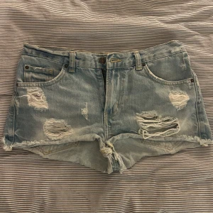 Ljusa jeansshorts från Alison Denim - Säljer ett par lågmidjade jeansshorts från Alison Denim med slitna detaljer och fransar. Perfekta för en avslappnad sommarlook. De har en klassisk femficksdesign och knappgylf🩵